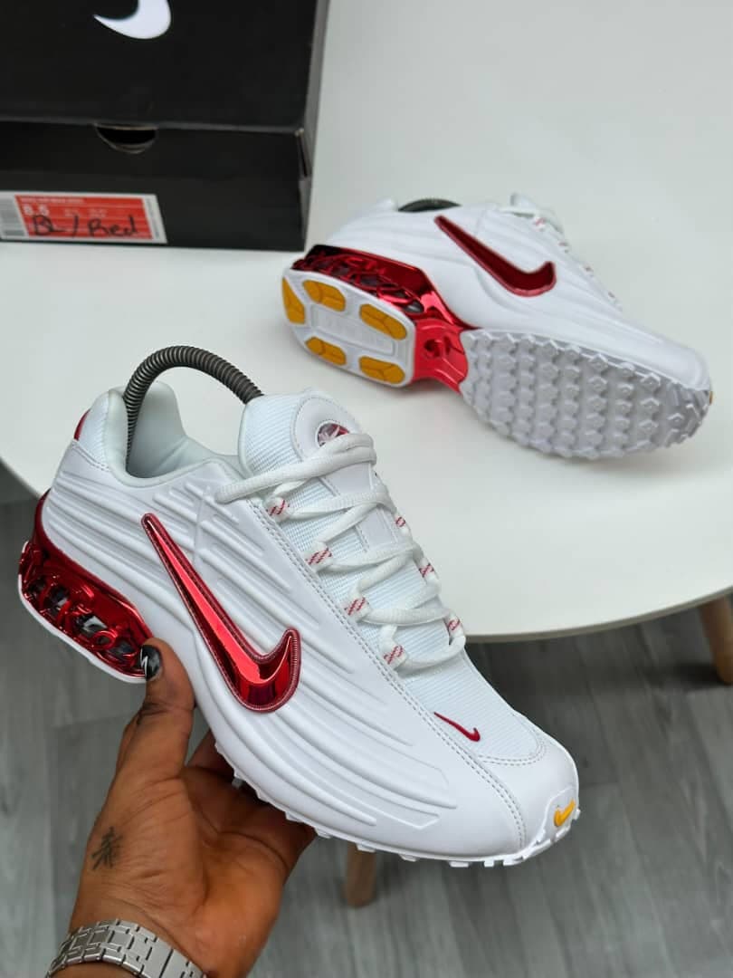 White and red Nike Air Max Plus sneakers held in hand showing red metallic details.