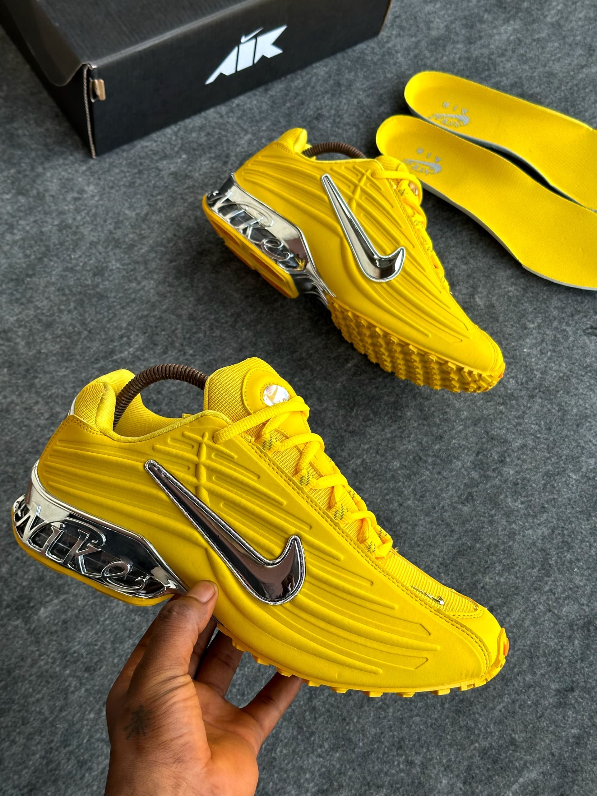 Bright yellow Nike Air Max Plus sneakers held in hand with yellow insoles and box.