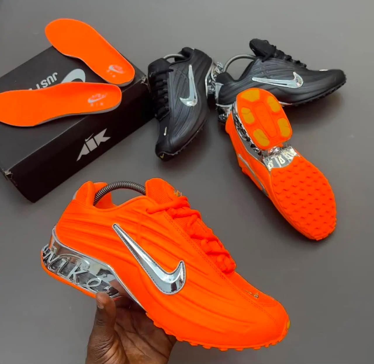 Orange and black Nike Air Max Plus sneakers displayed with box, insoles, and dice.