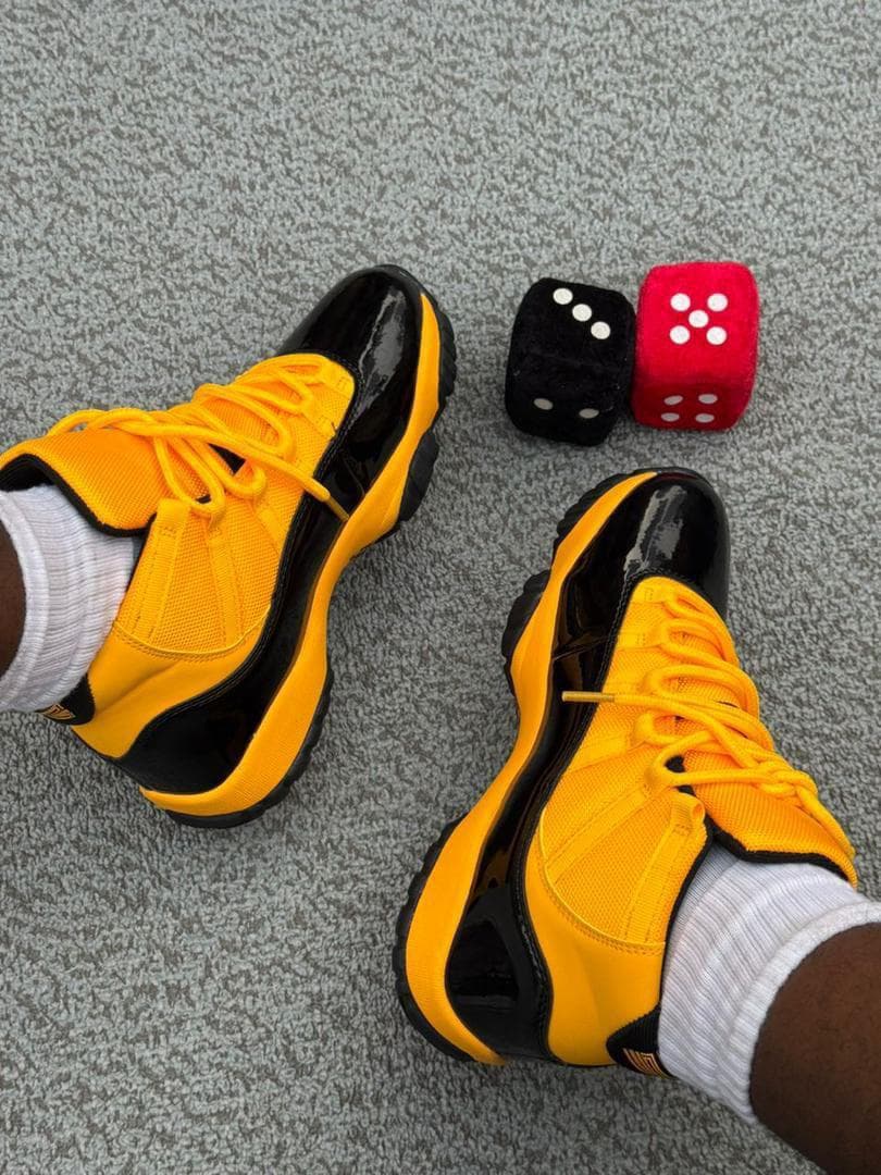 Yellow and black Air Jordan 11 sneakers worn on feet beside dice props.