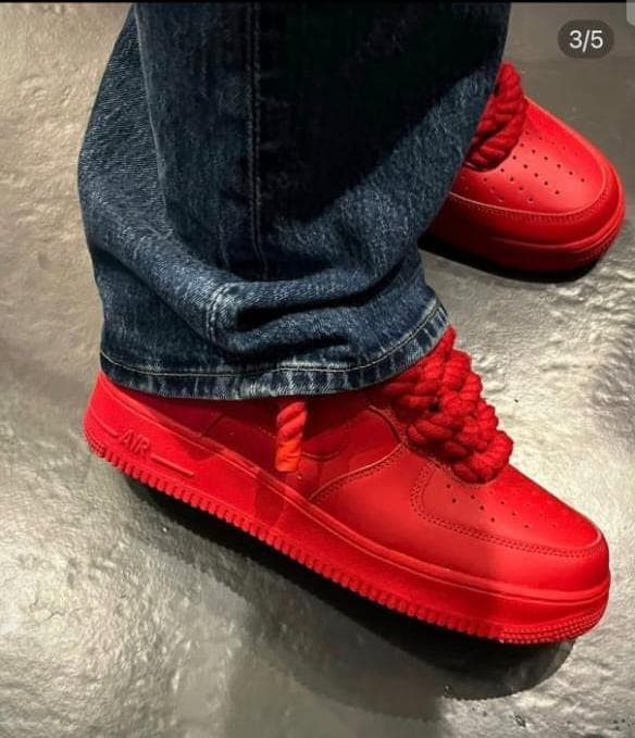 Red Nike Air Force 1 sneakers with thick rope laces worn with jeans on metallic surface.