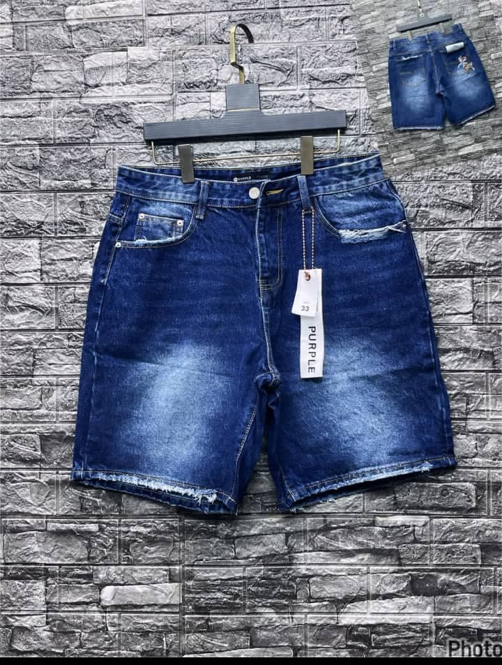 Blue denim shorts with rips on pockets and hanging tag displayed on brick wall.