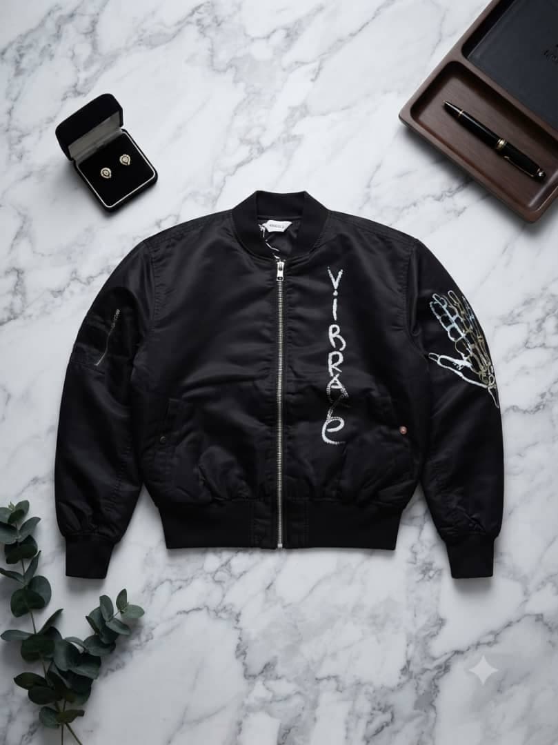 Black VIBRAXE bomber jacket with white embroidery and skeleton hand graphic on sleeve, laid flat on marble.