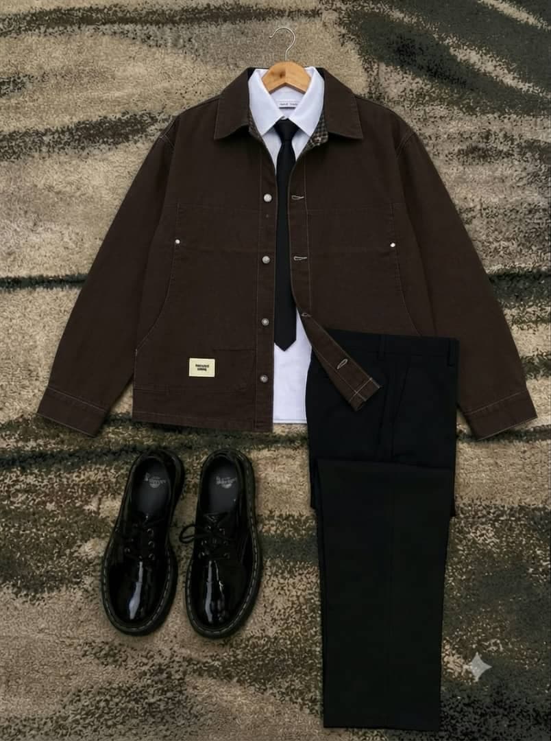 Brown denim jacket with white shirt, black tie, black trousers and shoes laid flat on textured rug.