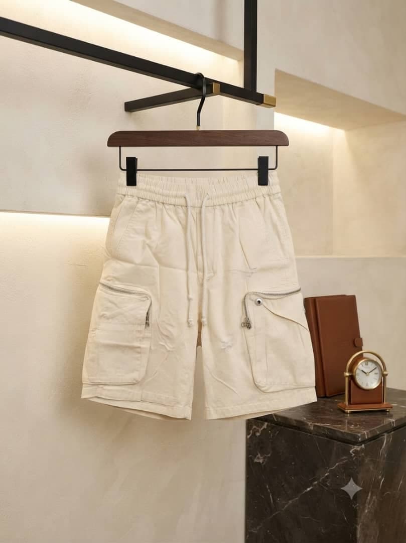 Cream unisex combat cargo shorts hanging on black hanger with minimalist decor.