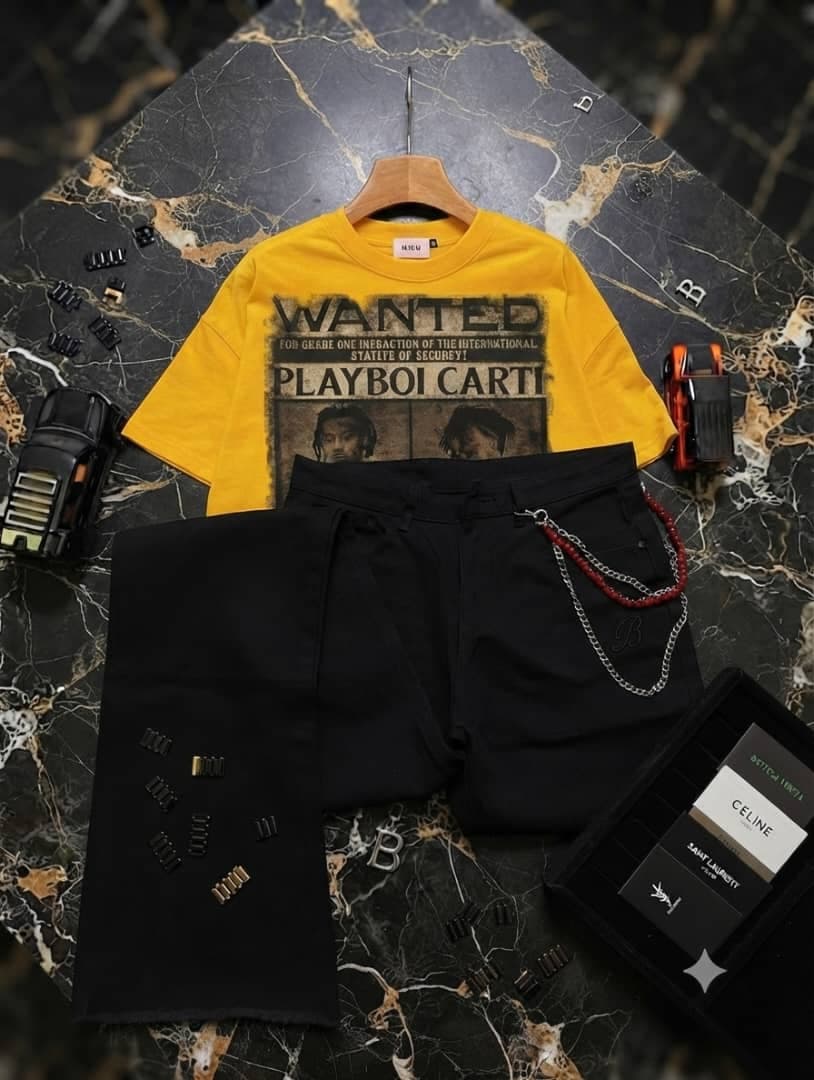 Yellow Playboi Carti wanted graphic t-shirt paired with black shorts with red and silver chain on marble background.