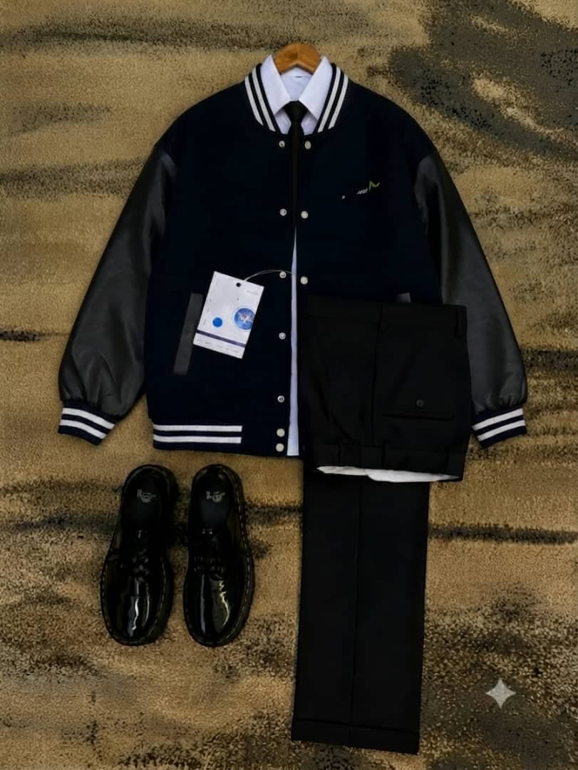 Navy varsity jacket with black sleeves styled with white shirt, black tie, trousers and shoes.
