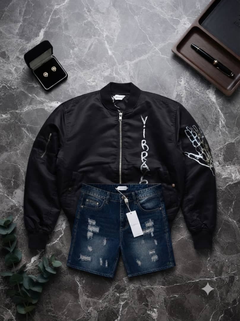 Black VIBBANE bomber jacket with white skeleton hand graphic and ripped denim shorts on marble background.