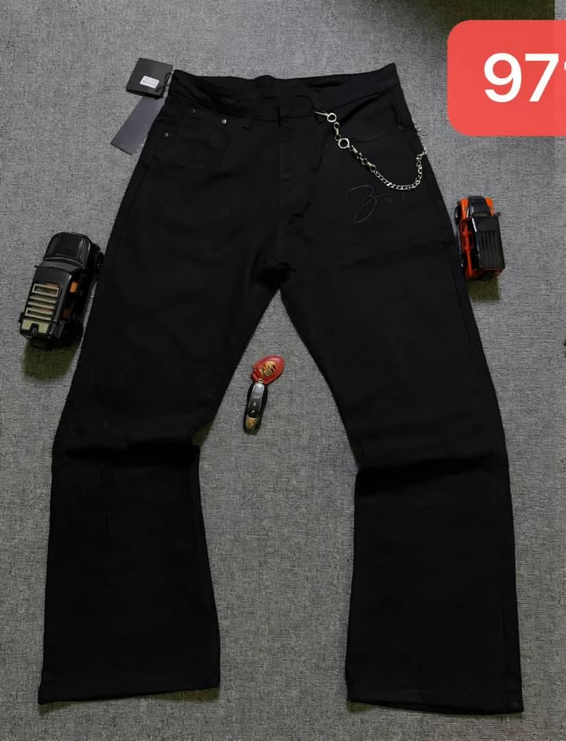 Black baggy jeans laid flat on gray surface with attached chain and props.