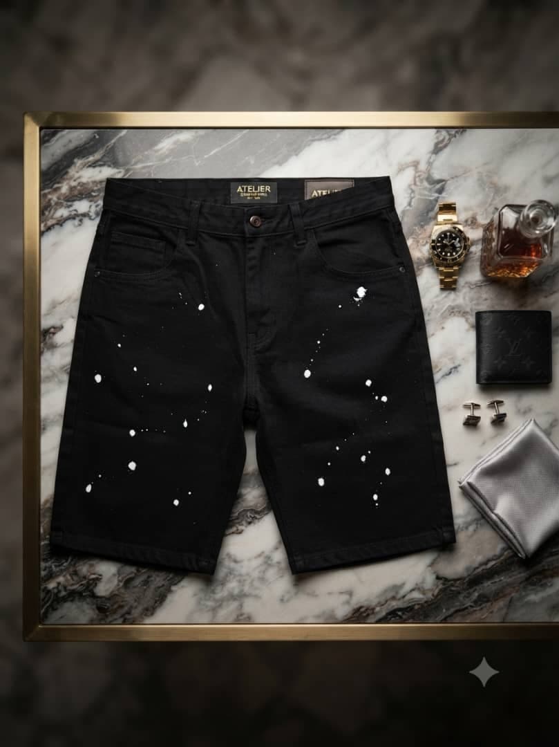 Black shorts with white splatter details styled on marble surface with luxury accessories.