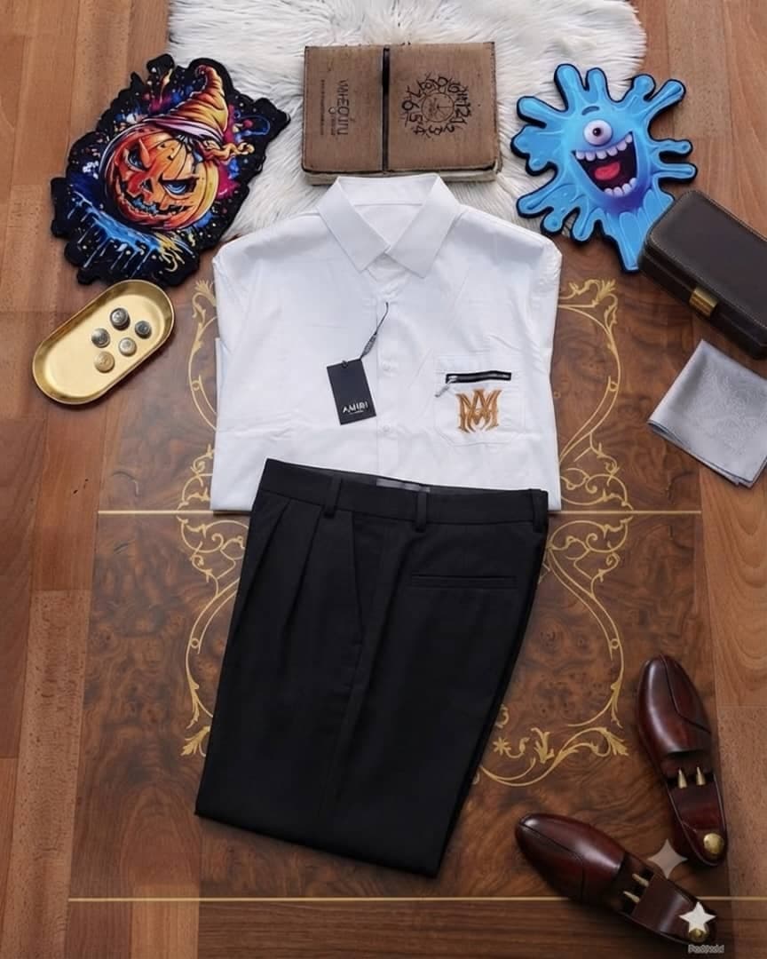 White Amiri shirt with MM pocket embroidery paired with black trousers on decorative floor with accessories.