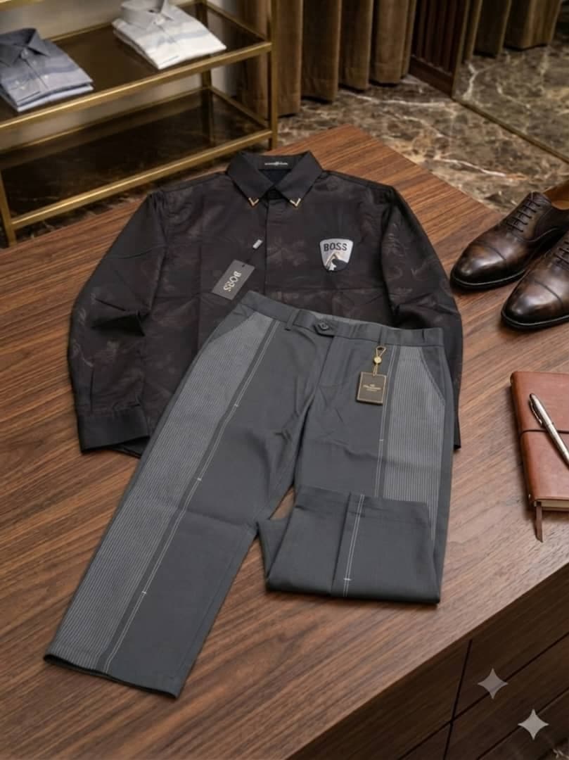 Black patterned Boss logo shirt paired with gray striped trousers on wooden surface with accessories.