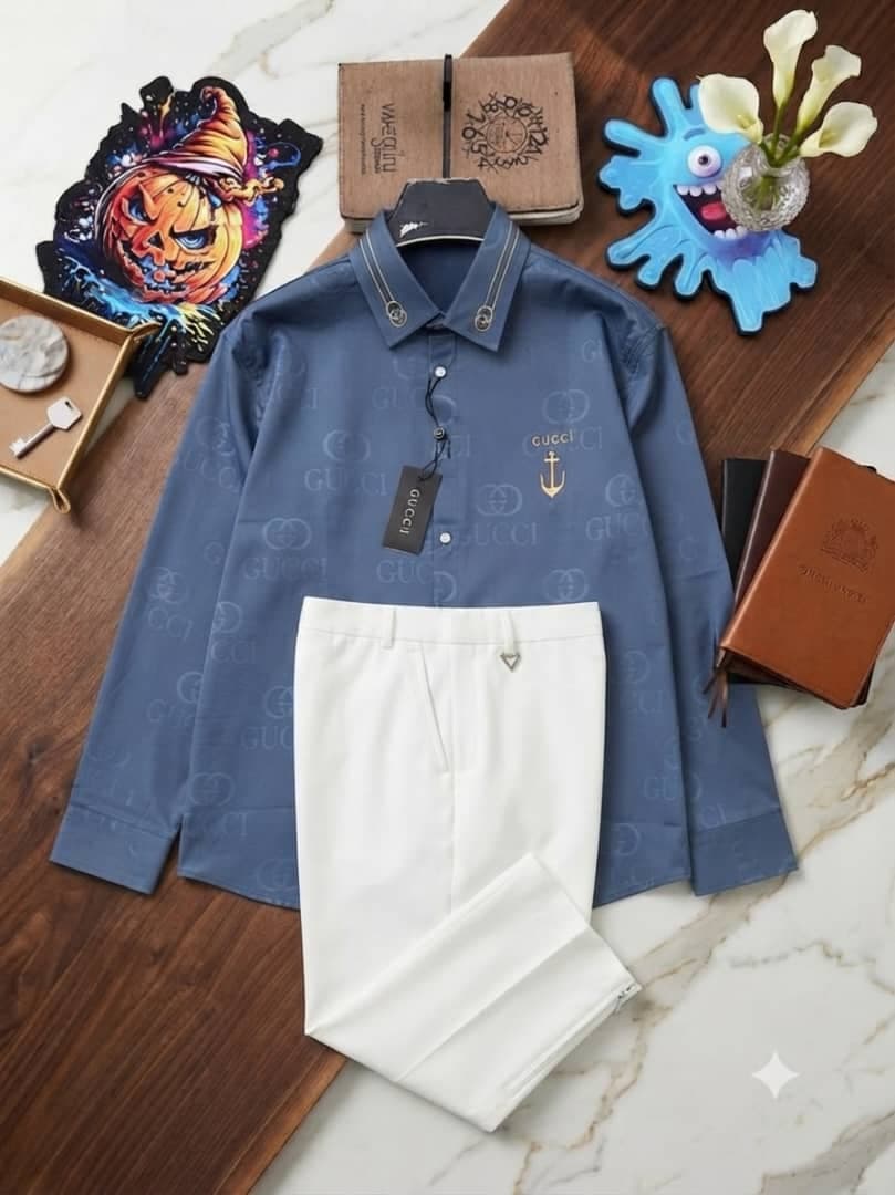 Blue monogram long-sleeve shirt with Gucci details paired with white trousers on marble and wood background.
