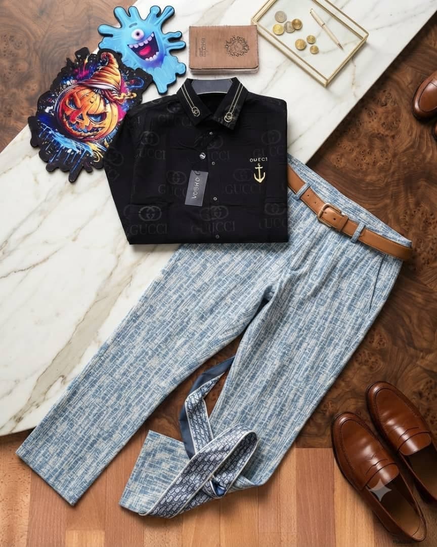 Black Gucci monogram long-sleeve shirt paired with light blue patterned trousers, brown belt and loafers on marble and wood surface.