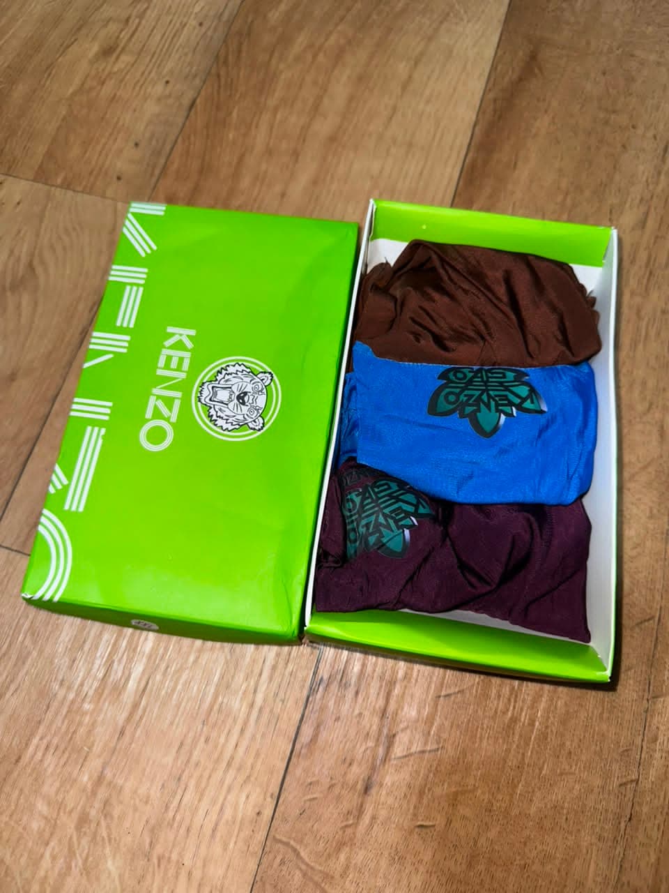 Open lime green Kenzo box containing three boxer briefs in brown, blue and purple with graphic prints.