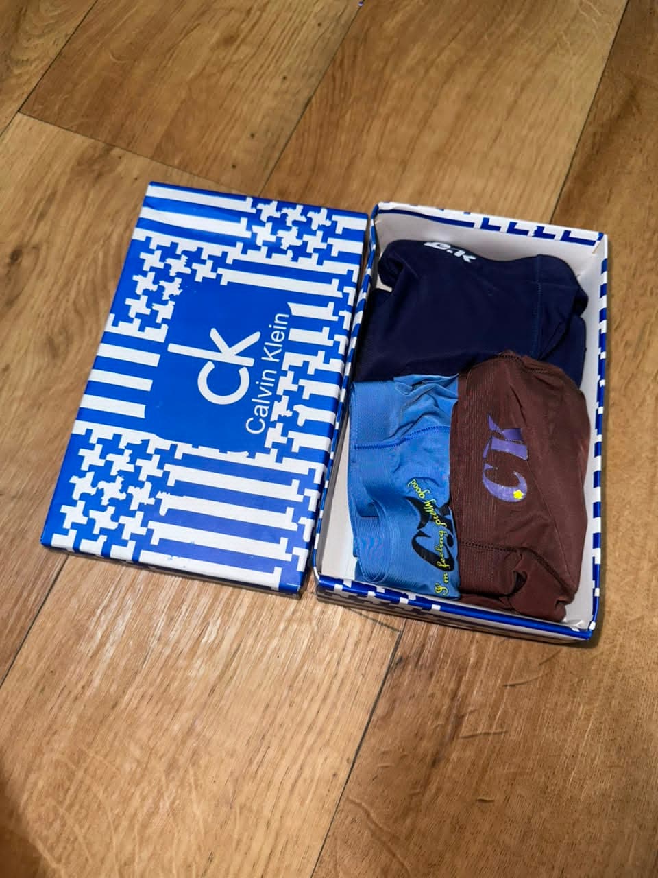 Open blue Calvin Klein box with three boxer briefs in navy, light blue and brown.