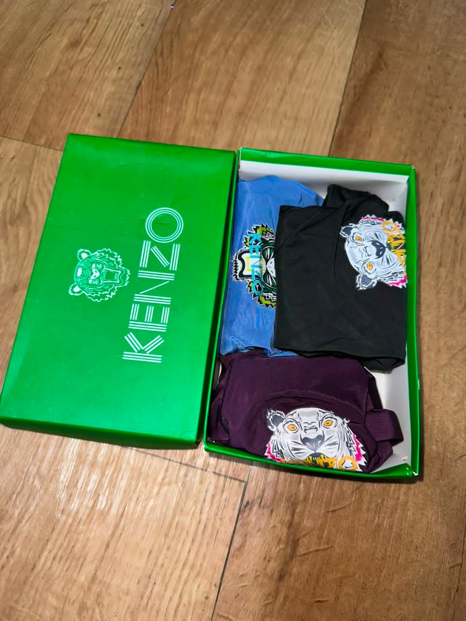 Open green Kenzo box displaying three folded boxer briefs in blue, black and purple with tiger graphics.