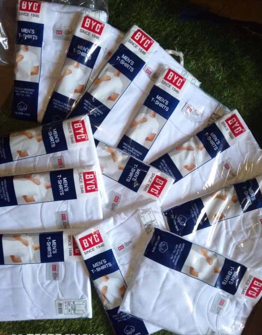 Multiple packaged BYC men's white t-shirts laid out on grass.