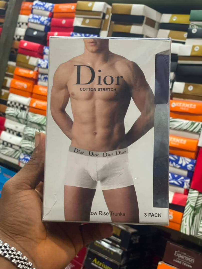 Hand holding Dior cotton stretch 3-pack low rise trunks packaging with model image and visible waistband detail.