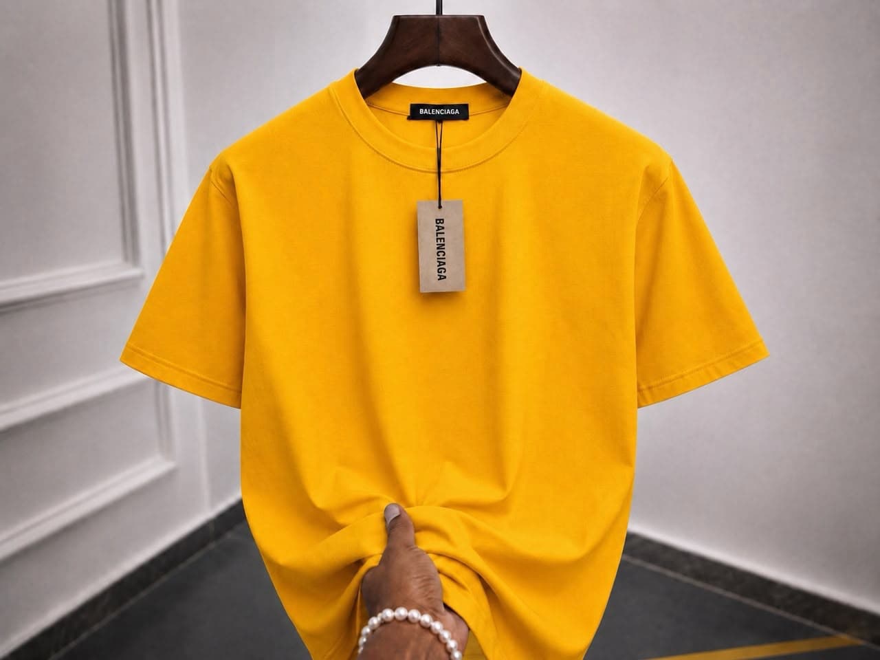 Plain yellow t-shirt on wooden hanger with hand holding the hem.