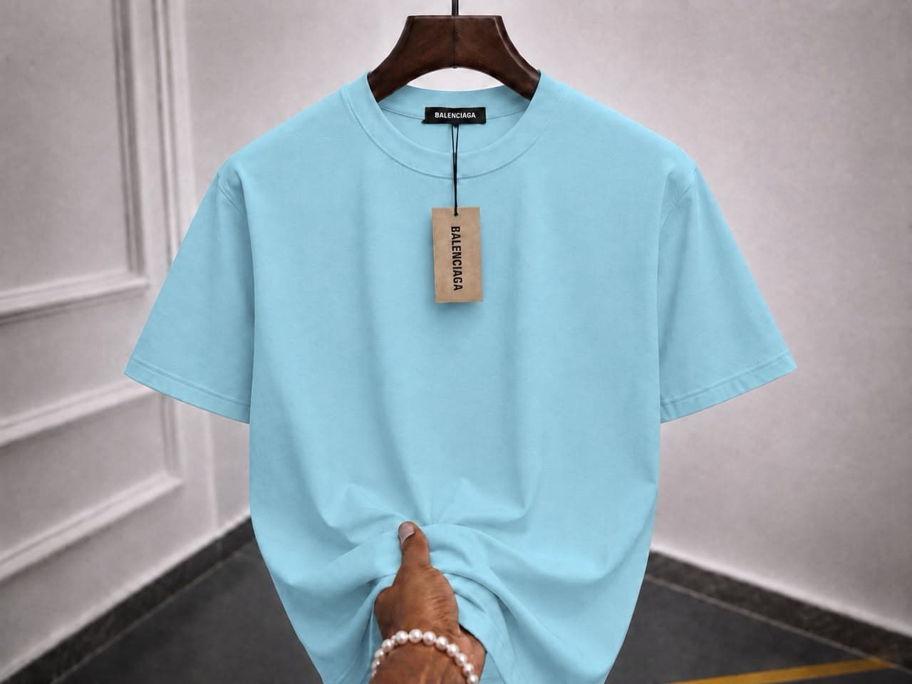 Plain light blue t-shirt on wooden hanger with hand holding the hem.