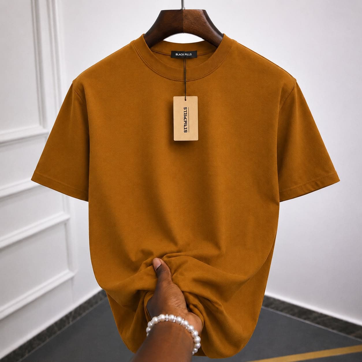 Plain brown t-shirt on wooden hanger with hand holding the hem.