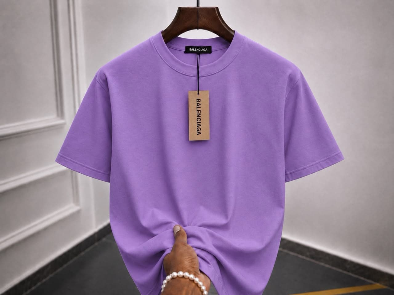 Plain purple t-shirt on wooden hanger with hand holding the hem.
