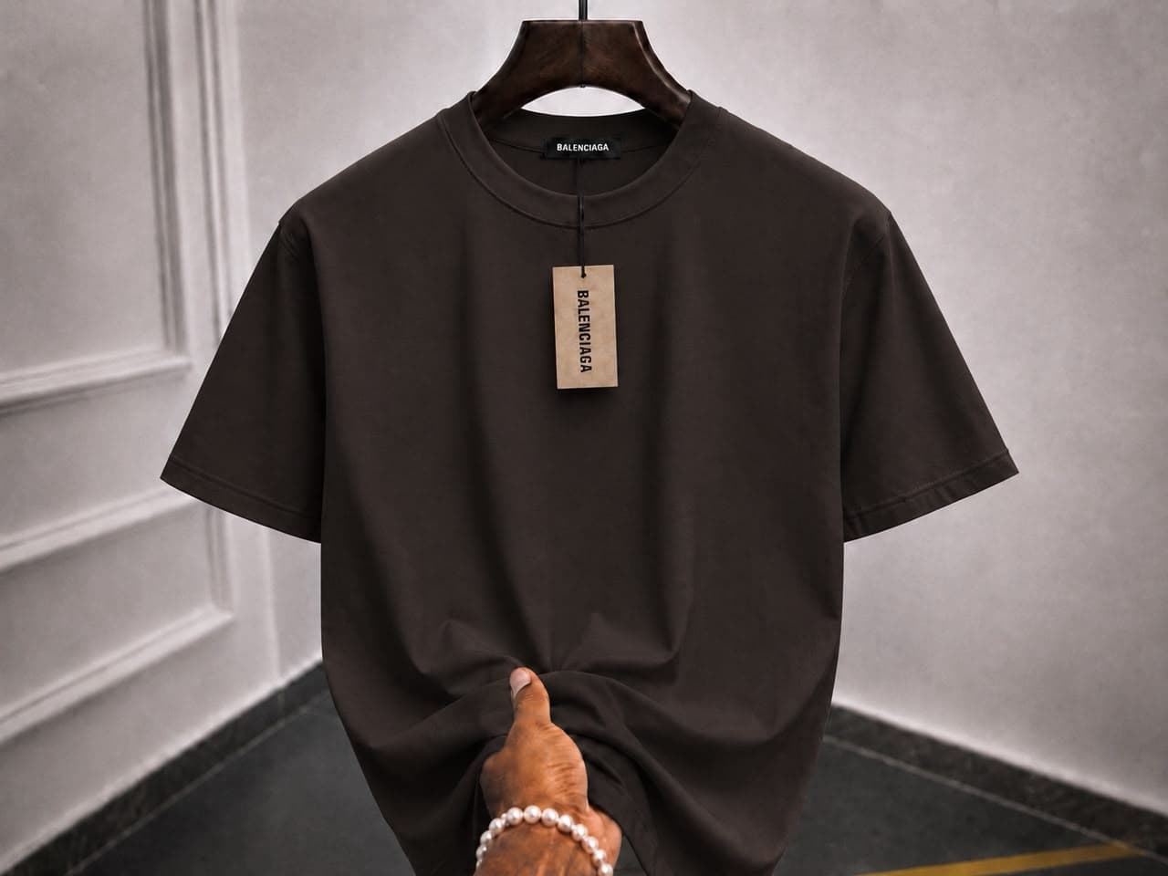 Plain black t-shirt on wooden hanger with hand holding the hem.