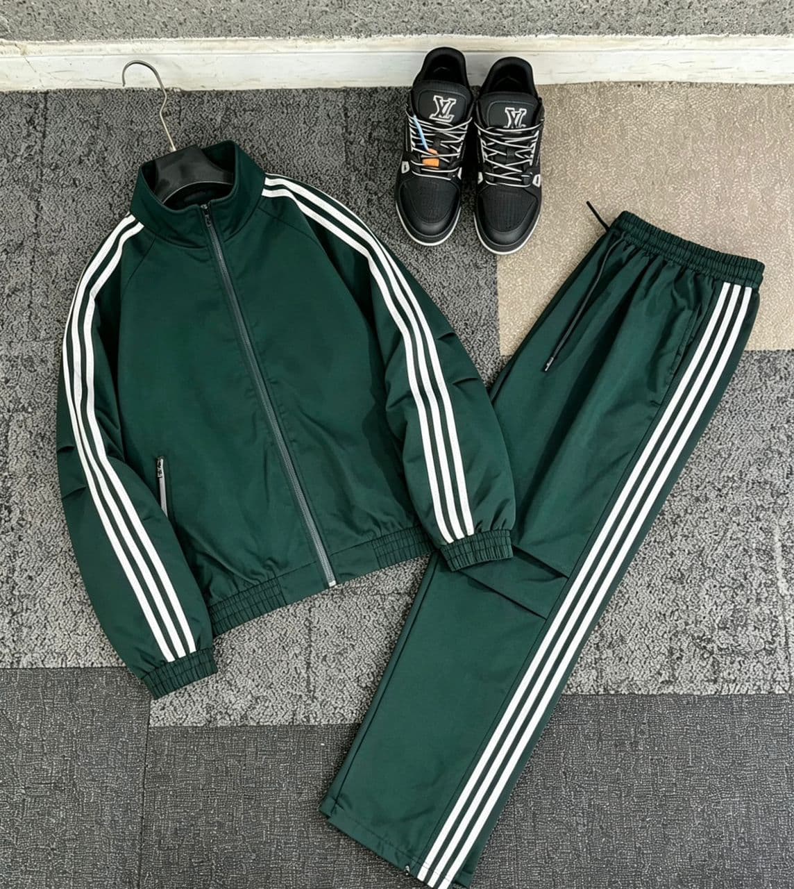 Green striped tracksuit set with zip jacket and pants laid out alongside black sneakers.