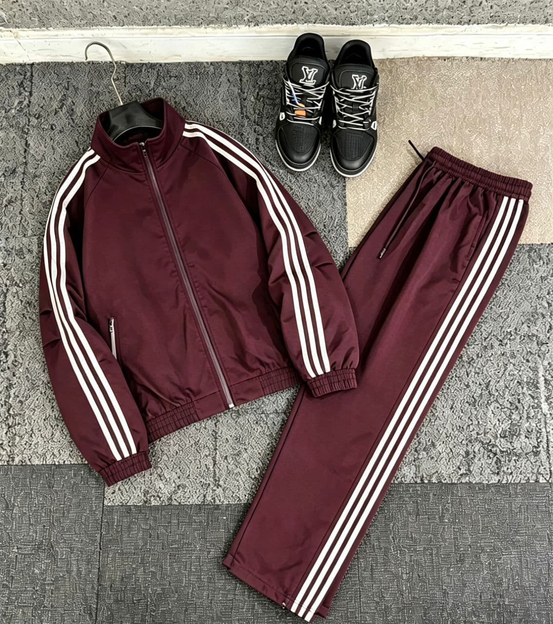 Burgundy striped tracksuit set with zip jacket and pants laid out alongside black sneakers.