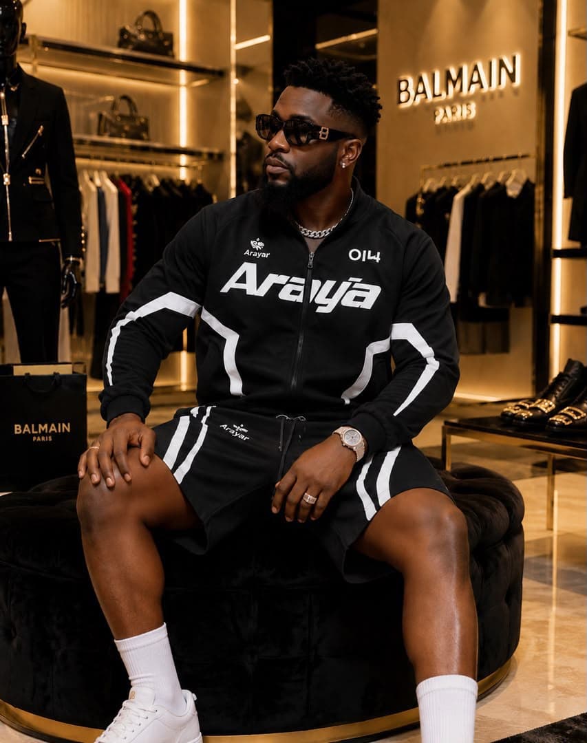 Man wearing black Araya zip-up jacket and shorts set while seated in luxury retail store.