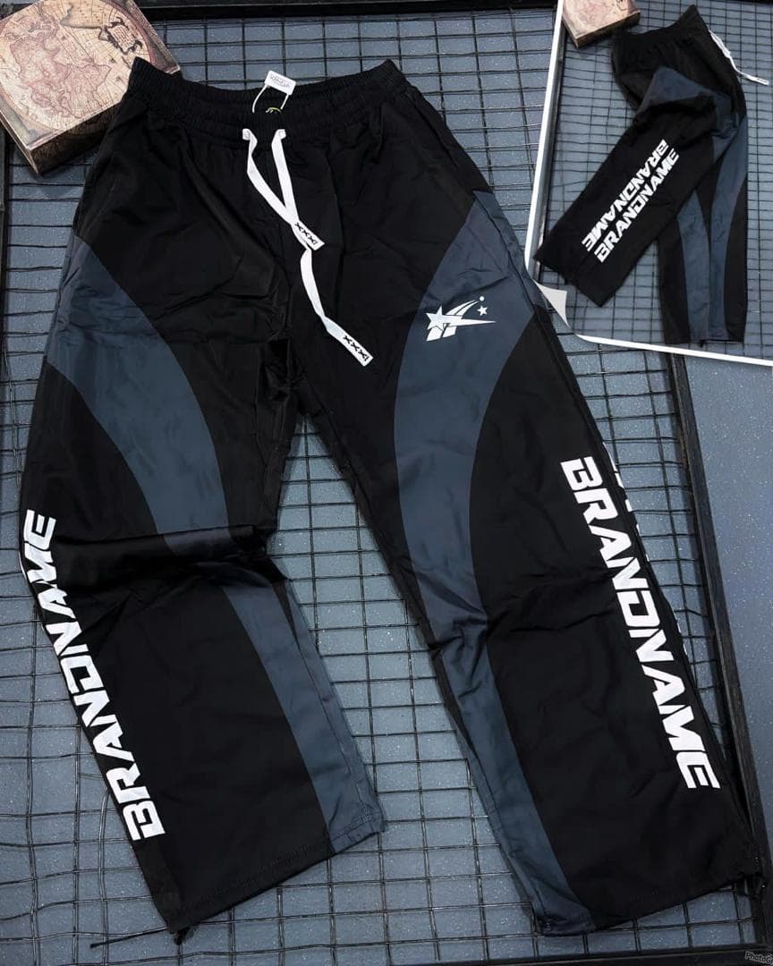 Flat lay of black and gray colorblock joggers showing vertical text, star logo and drawstring details.