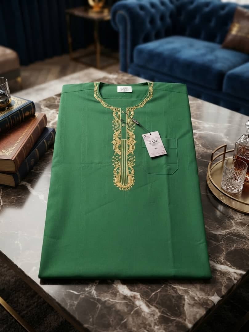Green jalabia with gold embroidery and tag on marble table.