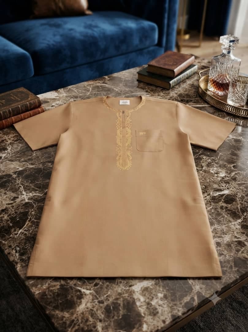 Beige jalabia with gold embroidery laid flat on marble surface.