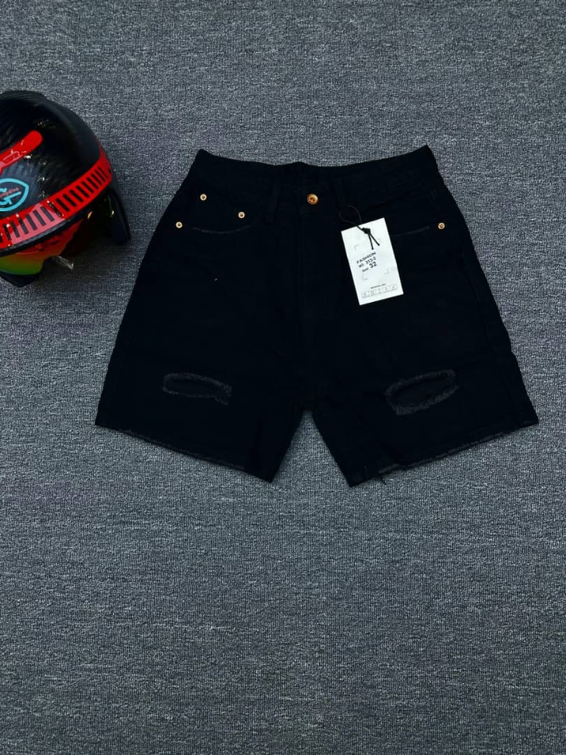 Black ripped denim shorts with thigh distressing, raw hem and attached tag, flat lay view.