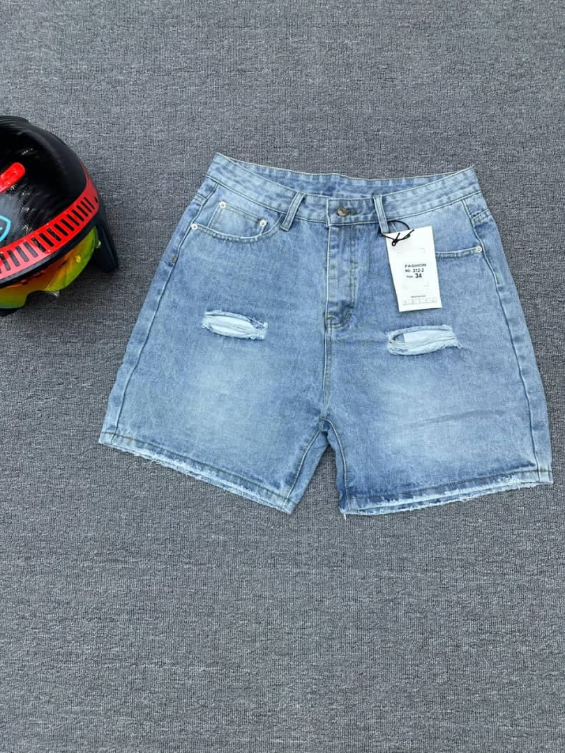 Light blue ripped denim shorts with thigh distressing and raw hem, flat lay on gray surface.