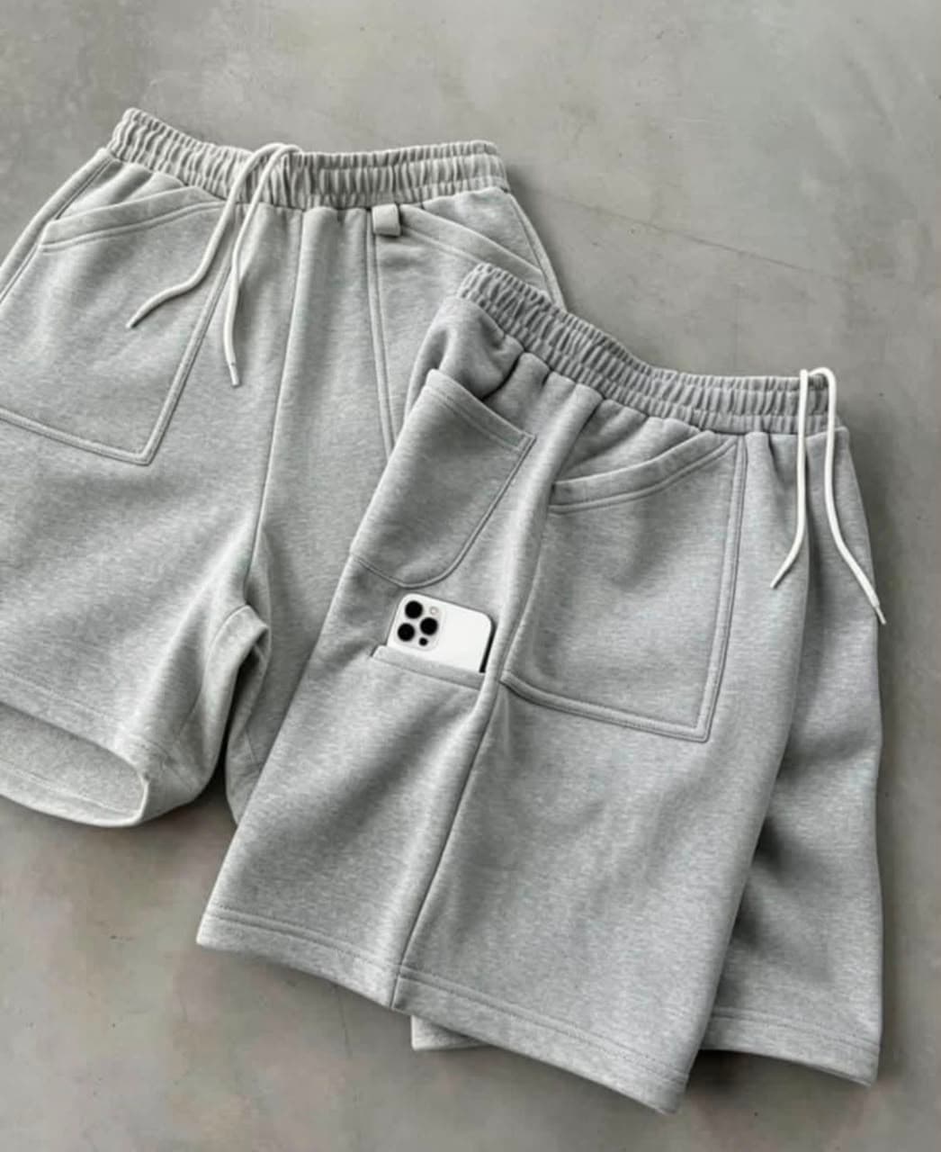 Flat lay of gray 3/4 fleece shorts showing drawstring and phone pocket.