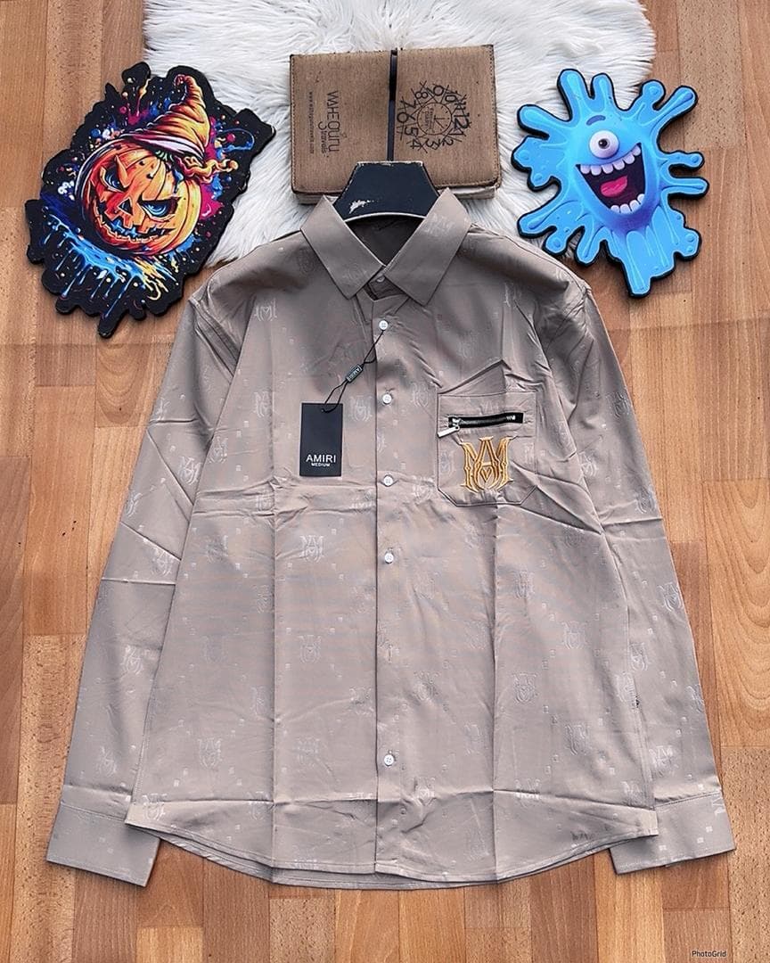 Beige Amiri monogram long sleeve shirt with zip pocket laid flat.