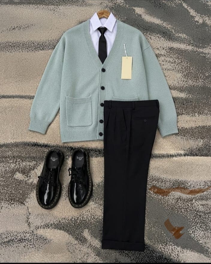 Flat lay of mint green button cardigan sweater with white shirt, tie, black trousers and shoes on patterned rug.