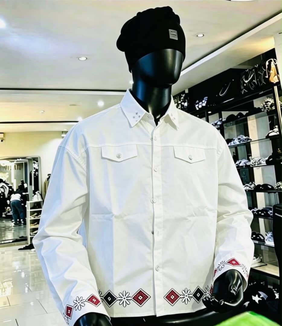 White long sleeve button-up shirt with embroidery on cuffs and hem, shown on mannequin.