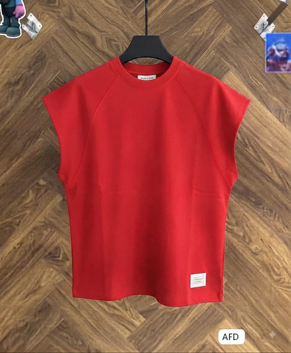 Red armless raglan t-shirt hanging on black hanger over wooden floor.