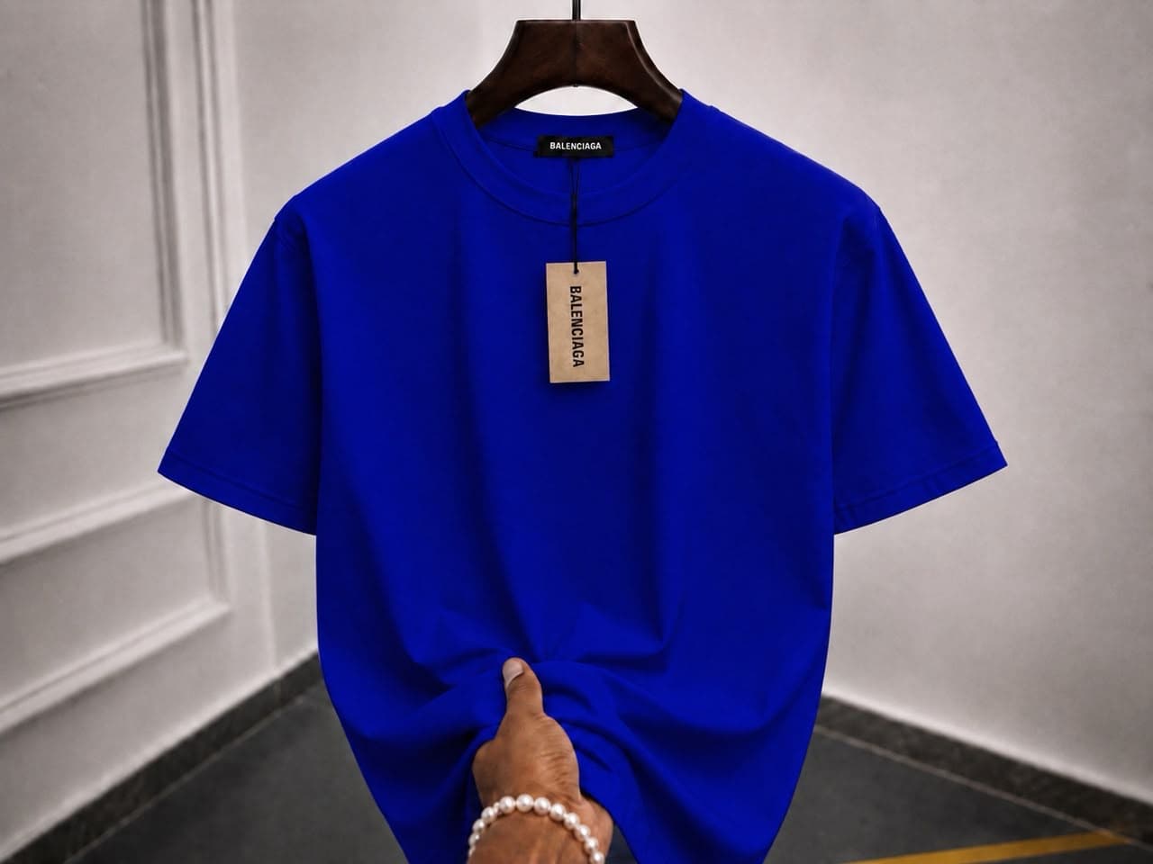 Royal blue oversized plain t-shirt on wooden hanger with hand holding the hem.