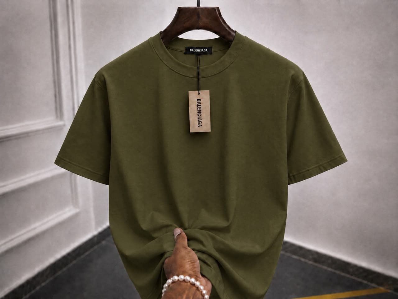 Olive green oversized plain t-shirt on wooden hanger with hand holding the hem.