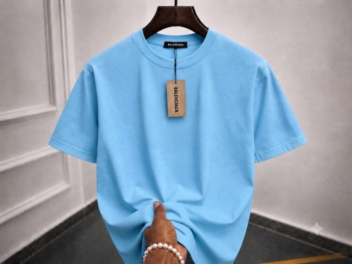 Light blue oversized plain t-shirt on wooden hanger with hand holding the hem.