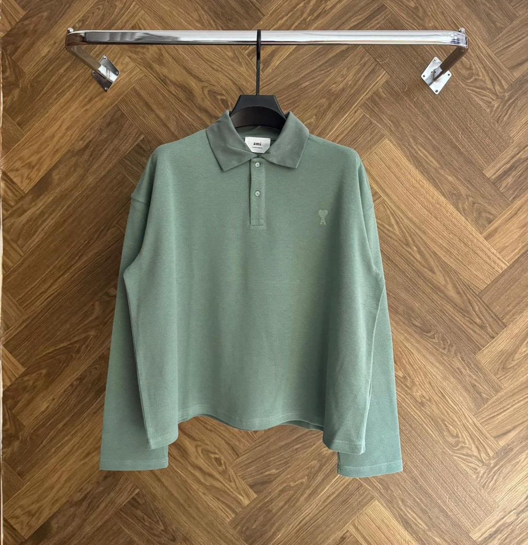 Green AMI long sleeve polo shirt hanging on rack against wooden floor.