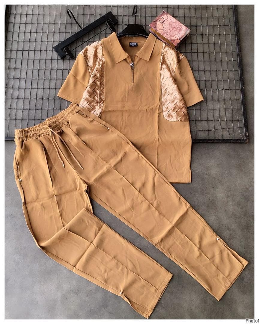Tan zip polo with woven pattern accents and matching trousers on gray background with props.
