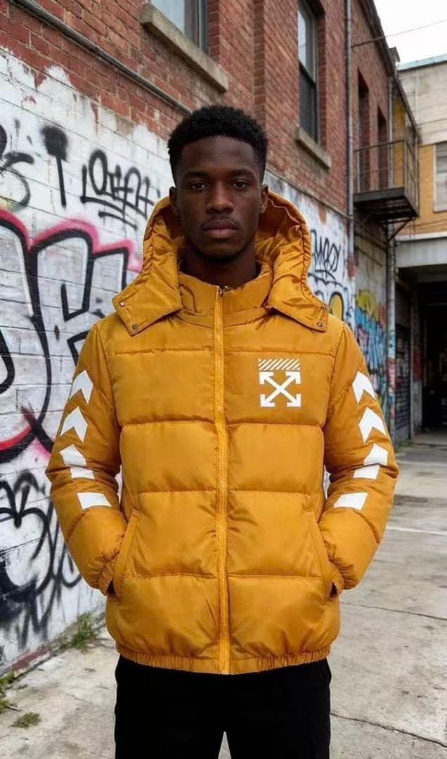 Man facing forward in yellow hooded puffer jacket with white arrow prints on chest and sleeves, hands in pockets.