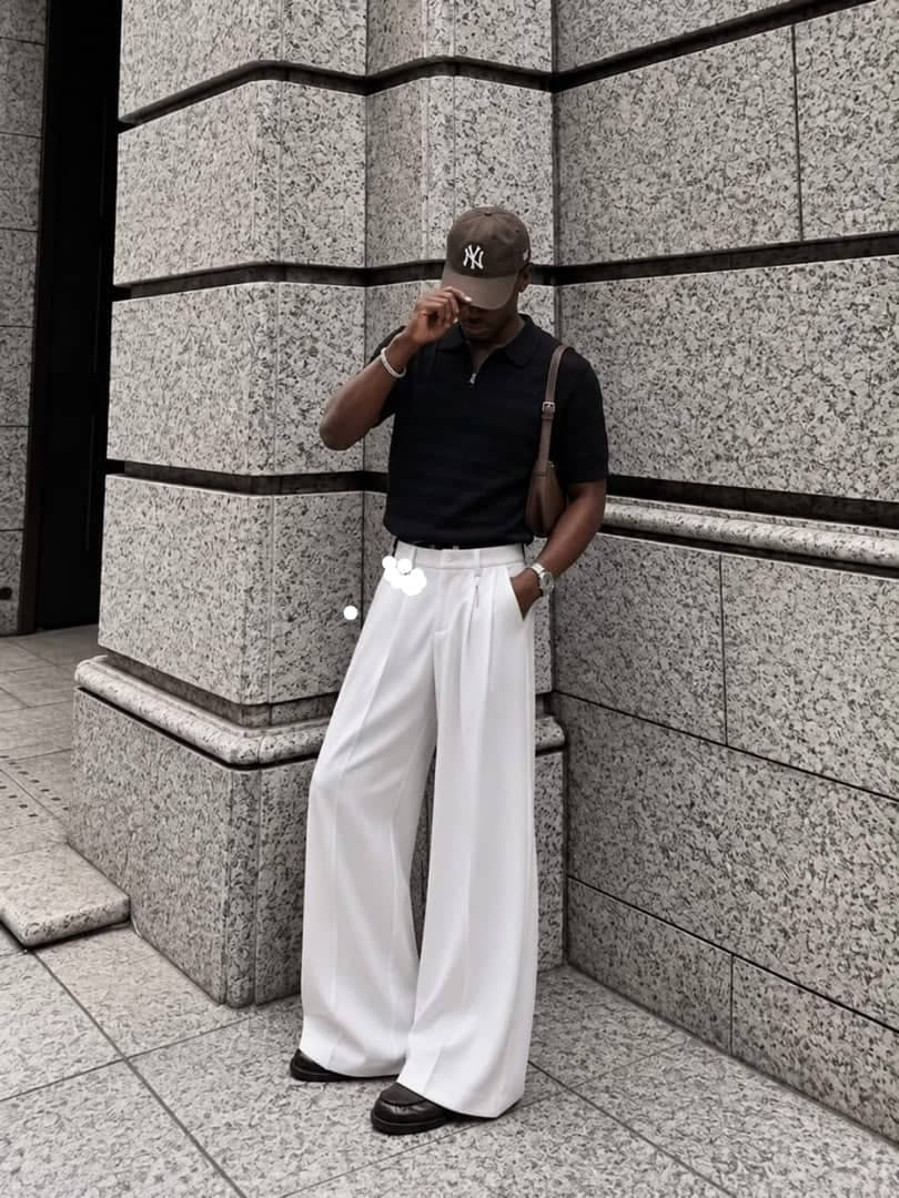 Model in white wide leg pleated flare trousers with black polo shirt.