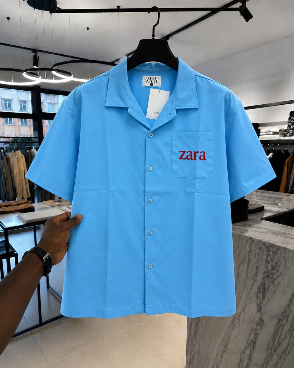 Light blue short-sleeve button-up shirt with red 'zara' embroidery on chest pocket.