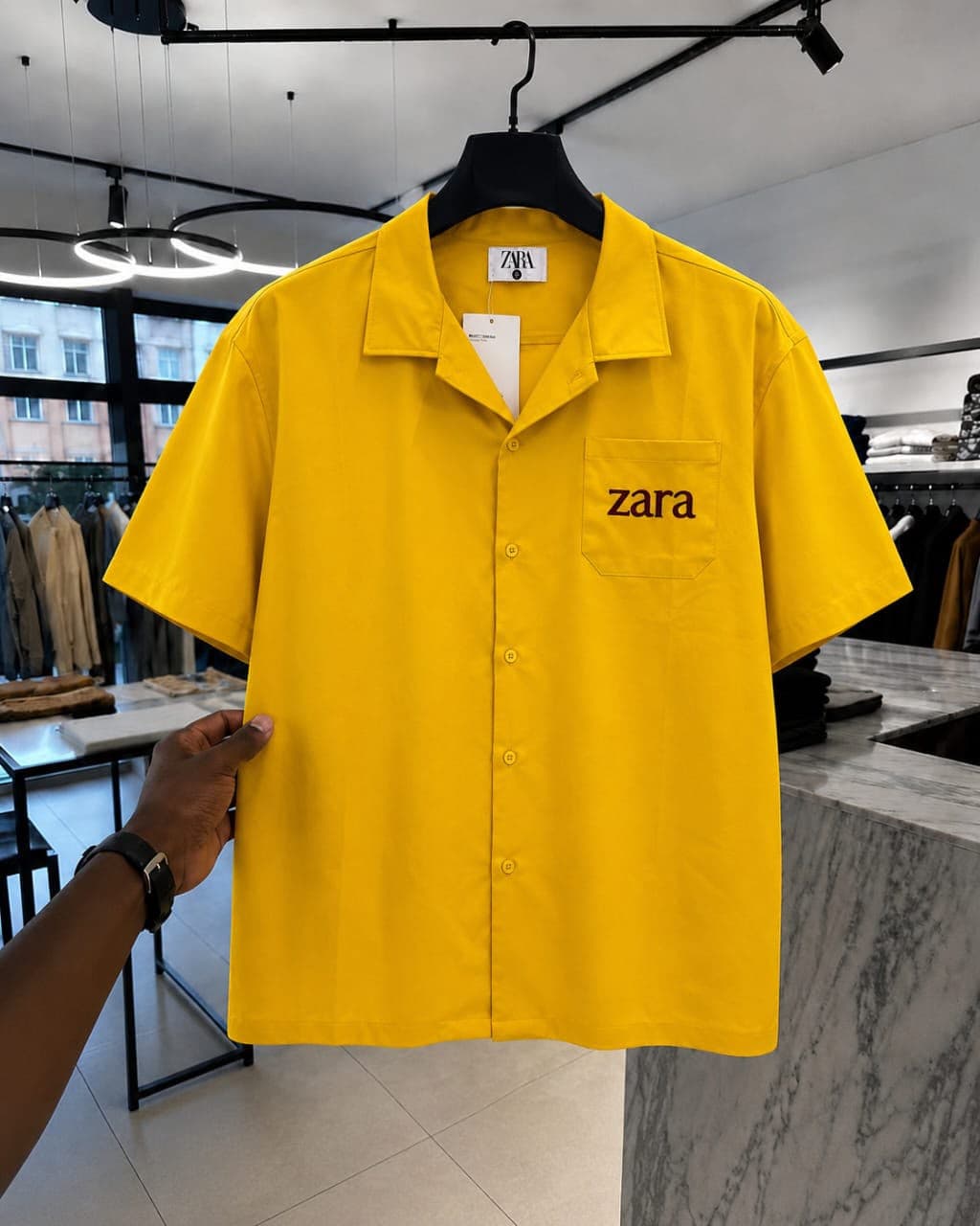 Yellow short-sleeve button-up shirt with dark 'zara' embroidery on chest pocket.